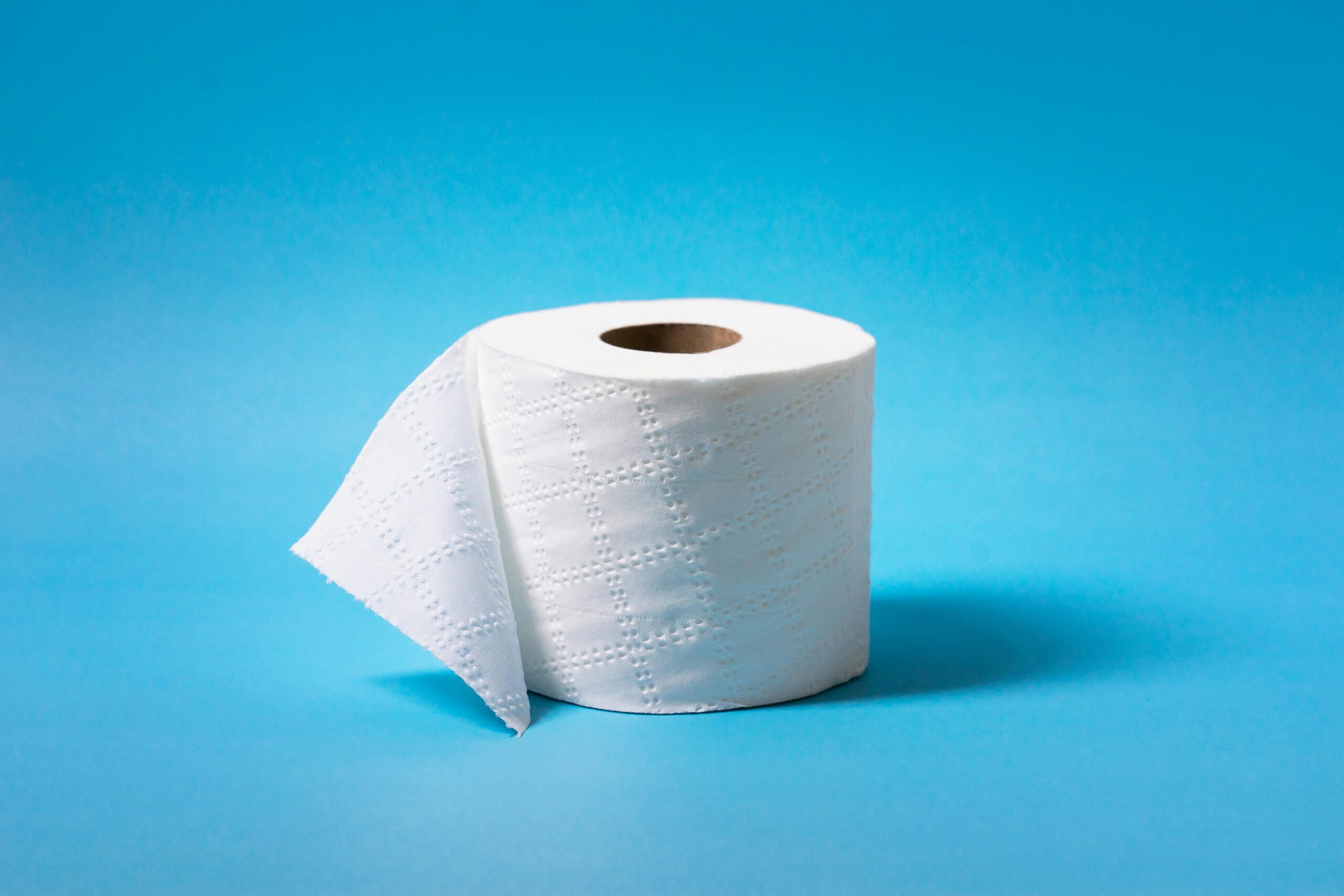 A single roll of toilet paper is isolated against a vibrant blue background, offering ample copy space.